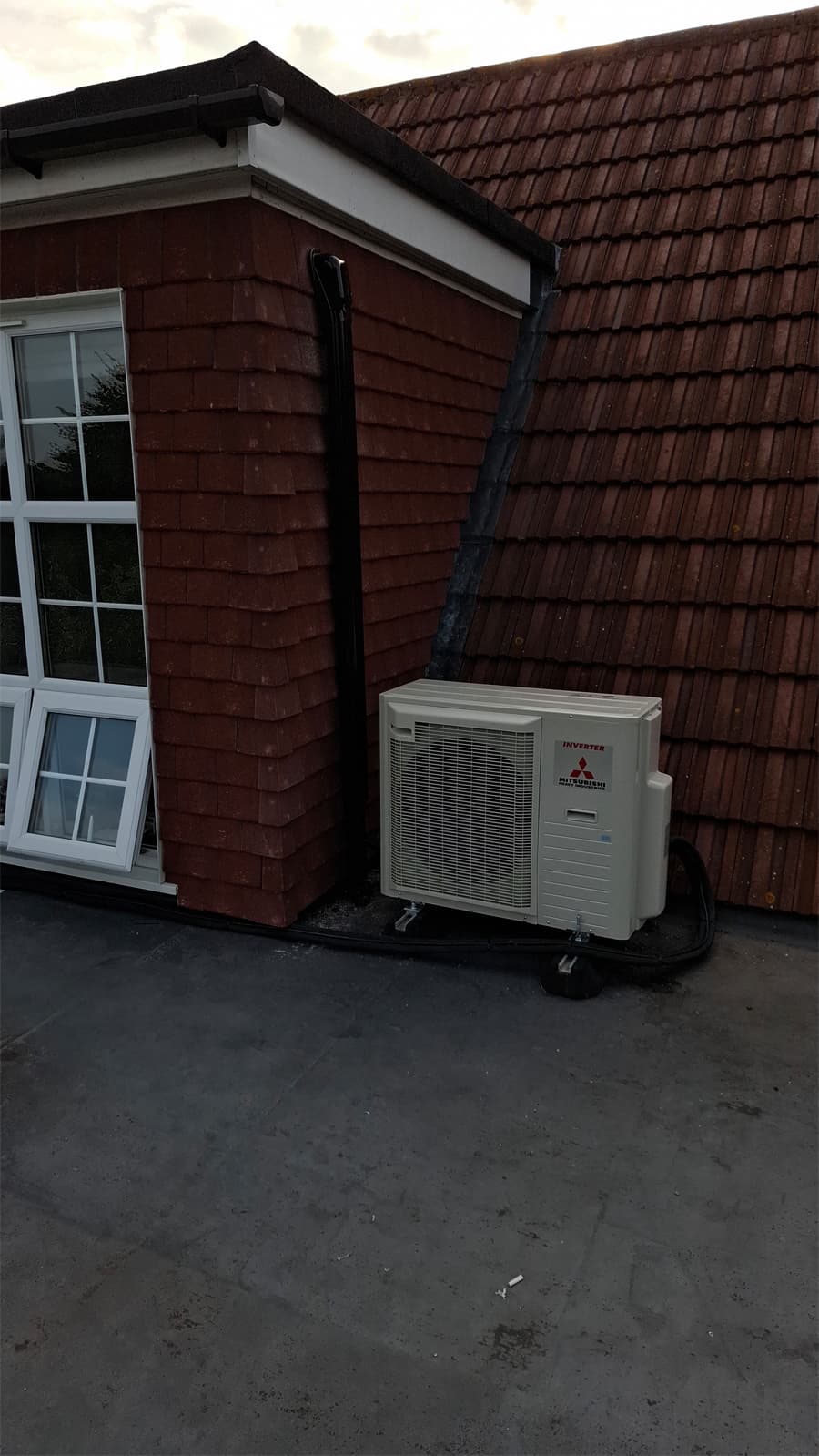 Mitsubishi outdoor heat pump unit beside tiled roof