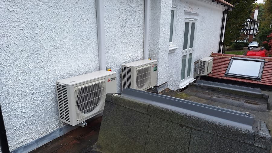 Twin outdoor air conditioning condenser units on white render wall
