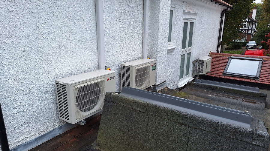 Twin outdoor air conditioning condenser units on white render wall