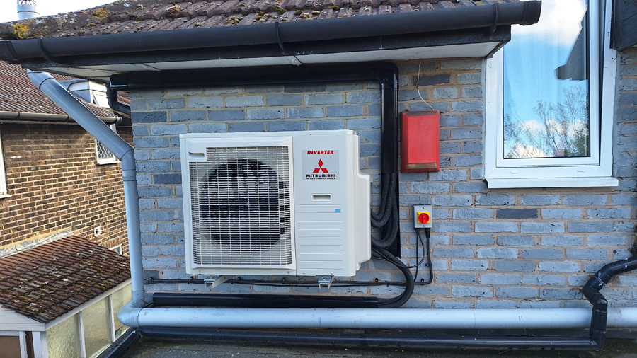 Mitsubishi air source heat pump outdoor unit on grey brick wall
